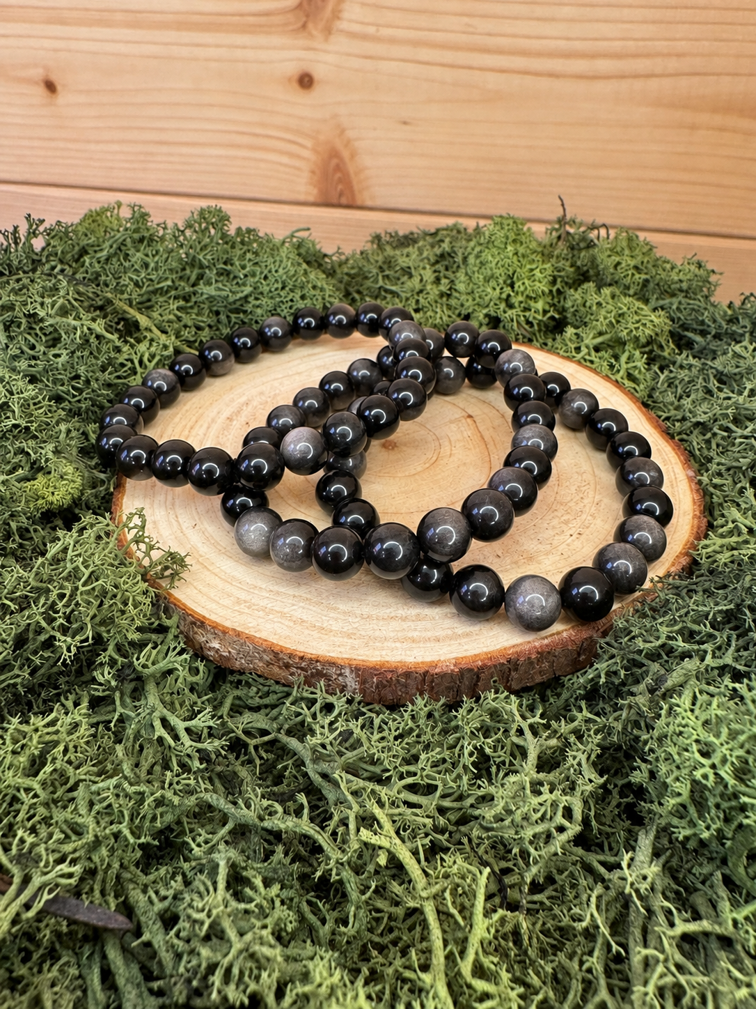 Three Silver Sheen Obsidian crystal bead bracelets displayed on natural wood